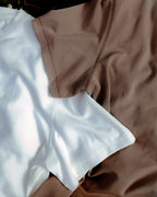 Stone Bark | A close-up of two folded fabric garments, one white and one taupe-brown, showing the texture and stitching of the material.