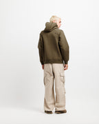 Olive Pit | On Model Full Back A model shown from the back wearing an olive green hooded jacket and beige cargo pants against a plain white studio background.