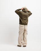 Olive Pit | On Model Full Back A person shown from the back wearing an olive green hoodie, beige cargo pants, and a beige bucket hat, standing against a plain light gray studio background.