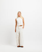 Cougar Milk | A blonde woman stands against a seamless white studio background wearing a sleeveless white crop top and matching wide-leg white trousers, paired with dark brown shoes.