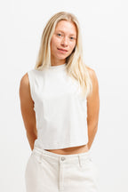 Cougar Milk | A blonde woman wearing a white sleeveless mock-neck crop top and off-white jeans, standing against a plain white studio background.