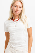 Cougar Milk | On Model Front A blonde woman wearing a white short-sleeve crewneck t-shirt, white jeans, and layered necklaces, including a red beaded necklace and a silver sunburst pendant, against a plain white background.