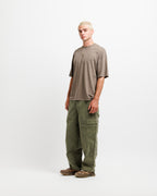 Cabin Smoke | A model stands in profile wearing an oversized taupe-brown short-sleeve t-shirt, olive green cargo pants, and brown shoes against a plain white studio background.