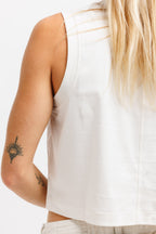 Cougar Milk | A close-up back view of a woman wearing a white sleeveless crop top and light-colored pants against a plain white background.