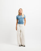 Frostbite Blue | On Model Full Front A blonde woman stands against a plain white studio background wearing a fitted blue short-sleeve top, off-white wide-leg pants, and gray sneakers.