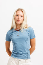 Frostbite Blue | On Model Front A blonde woman wearing a light blue short-sleeve athletic t-shirt and off-white pants, standing against a plain white background.