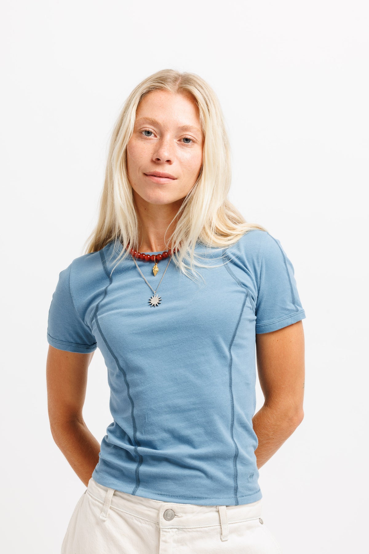 A blonde woman wearing a light blue short-sleeve athletic t-shirt and off-white pants, standing against a plain white background.