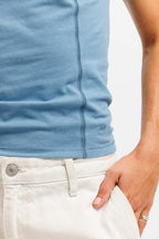 Frostbite Blue | On Model Front Detail 2 Close-up of a person wearing a light blue ribbed knit top tucked into off-white pants, with a hand resting in the pocket. A small embroidered logo is visible near the lower right side of the shirt.