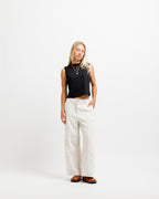 Ink Black | A woman stands against a plain white studio background wearing a sleeveless black crop top, off-white wide-leg pants, and brown shoes.