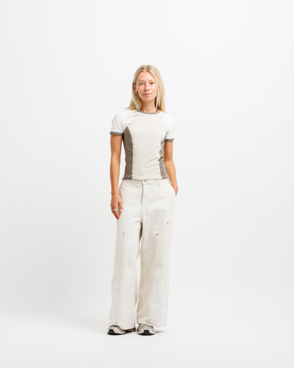 A woman modeling a beige short-sleeve knit top with brown side panels and matching beige wide-leg trousers, standing against a plain white studio background.