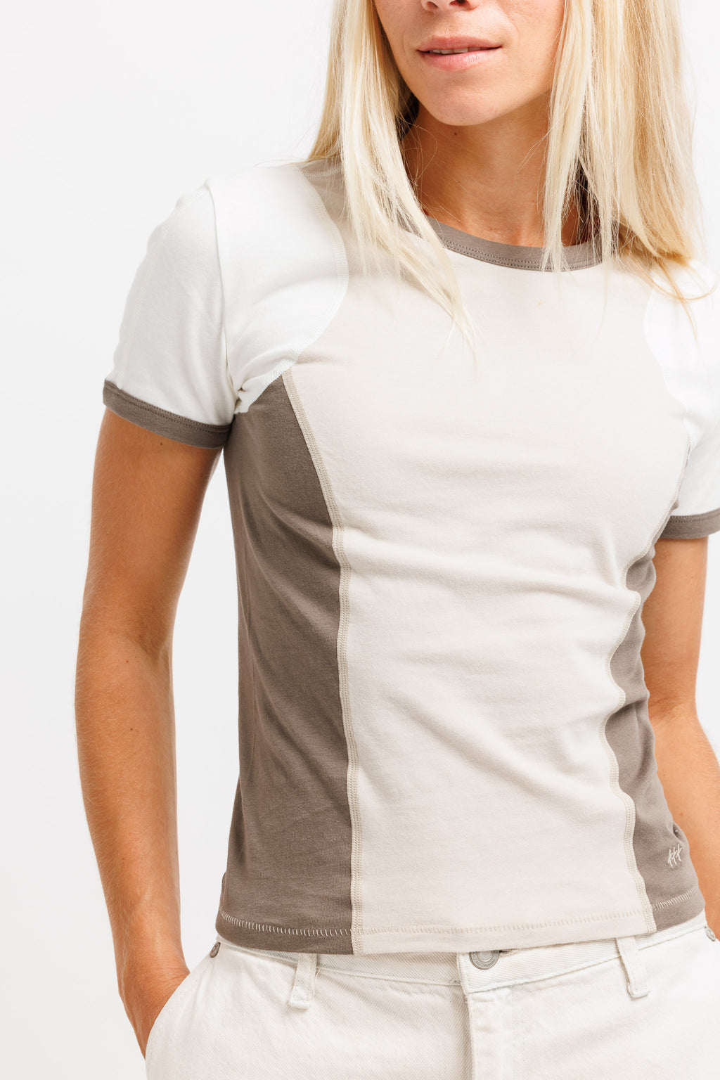 A woman wearing a short-sleeve colorblock t-shirt with a white and beige design, paired with light beige pants, against a plain white background.