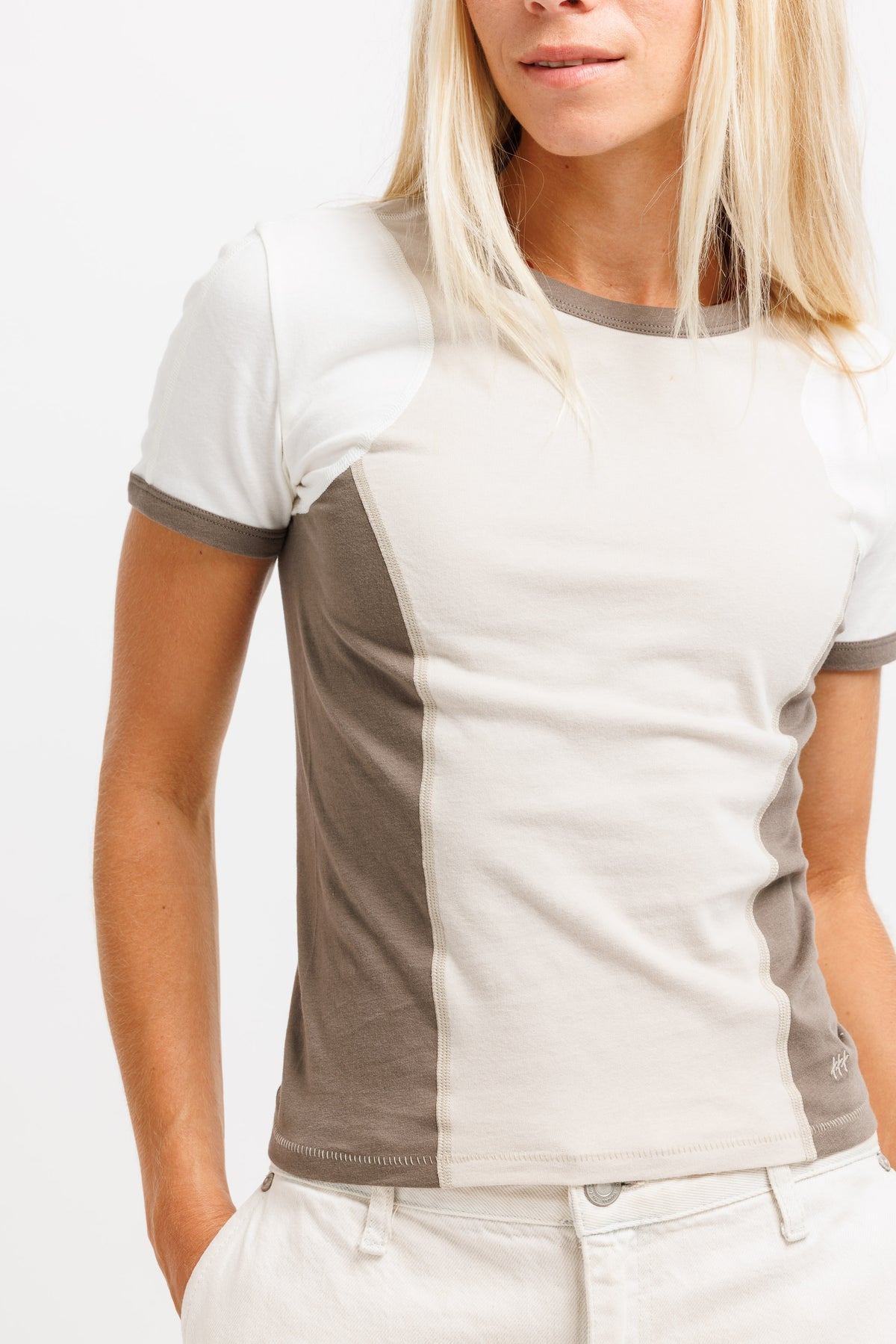A woman wearing a short-sleeve colorblock t-shirt with a white and beige design, paired with light beige pants, against a plain white background.