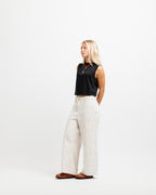 Ink Black | A woman stands in profile wearing a black sleeveless crop top, off-white wide-leg pants, and brown shoes against a plain white studio background.