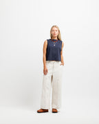 Deepwater Navy | A woman stands against a plain white studio background wearing a sleeveless navy top, wide-leg off-white pants, and brown shoes.