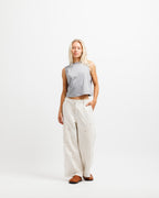 Chiseled Stone | A woman stands against a plain white studio background wearing a light gray sleeveless cropped top, off-white wide-leg pants, and brown shoes.