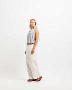 Chiseled Stone | A woman stands in profile wearing a light gray sleeveless crop top, off-white wide-leg pants, and brown shoes against a plain white studio background.