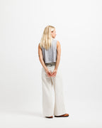 Chiseled Stone | A woman with long blonde hair is shown from behind wearing a sleeveless gray top, wide-leg cream pants, and brown shoes against a plain white studio background.