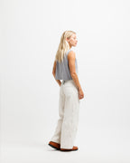 Chiseled Stone | A woman stands in profile wearing a gray sleeveless crop top, off-white wide-leg pants, and brown shoes against a clean white studio background.
