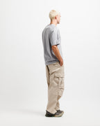 Chiseled Stone | On Model Full Side A man with short blonde hair stands in profile wearing a light gray short-sleeve t-shirt, beige cargo pants, and dark sneakers against a plain white studio background.
