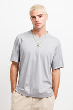 Chiseled Stone | On Model Front A man with platinum blonde hair wearing a light gray v-neck t-shirt and beige pants, standing against a plain white studio background.