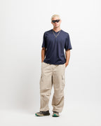 Deepwater Navy | On Model Full Front A model stands against a light gray studio background wearing a navy blue short-sleeve t-shirt, beige cargo pants, and dark sunglasses.