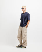 Deepwater Navy | On Model Full Side A man wearing a navy blue t-shirt, beige cargo pants, and sunglasses, standing in profile against a plain white studio background.