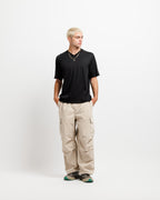 Ink Black | On Model Full Front A man modeling a black short-sleeve t-shirt, beige cargo pants, and sneakers, standing against a plain white studio background.