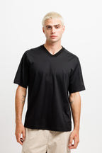 Ink Black | On Model Front A man with platinum blonde hair wearing a black short-sleeve V-neck t-shirt and beige cargo shorts, standing against a light gray studio background.