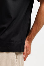 Ink Black | On Model Back Detail Close-up of a person wearing a black short-sleeve t-shirt and light beige shorts against a plain white background.