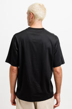 Ink Black | On Model Back A man with short blonde hair is shown from the back wearing a black short-sleeve crewneck t-shirt and light beige pants against a plain white background.