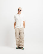 Cougar Milk | On Model Full Front A model stands against a plain white studio background wearing a white short-sleeve polo shirt, beige cargo pants, and dark sneakers.