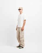 Cougar Milk | On Model Full Side A man wearing a white short-sleeve polo shirt, beige cargo pants, and black sunglasses, standing in profile against a plain white studio background.