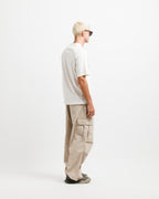 Cougar Milk | On Model Full Side 2 A man with blonde hair and sunglasses stands in profile wearing a white t-shirt, beige cargo pants, and dark sneakers against a plain white studio background.