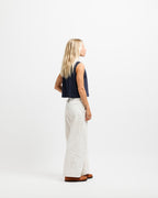 Deepwater Navy | A woman with blonde hair is shown from a side-back angle, wearing a dark navy sleeveless crop top, off-white wide-leg pants, and brown shoes, standing against a plain white studio background.