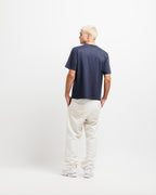 Deepwater Navy | On Model Full Back A man with platinum blonde hair is shown from behind wearing a navy blue t-shirt, off-white corduroy pants, and white sneakers, standing against a plain white studio background.