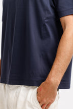 Deepwater Navy | On Model Side Detail Close-up of a person wearing a navy blue short-sleeve t-shirt and off-white trousers, with the hand in the trouser pocket visible against a plain white background.