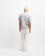Chiseled Stone | On Model Full Back A man with short blonde hair is shown from behind wearing a light gray crewneck t-shirt, off-white trousers, and white sneakers, standing against a plain white studio background.