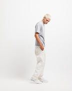 Chiseled Stone | On Model Full Side A model with platinum blonde hair stands in profile wearing a light gray crewneck t-shirt, off-white wide-leg trousers, and white sneakers against a plain white studio background.