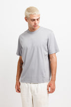 Chiseled Stone | On Model Front A man with platinum blonde hair wearing a light gray short-sleeve crewneck t-shirt and off-white trousers, standing against a plain white studio background.