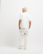Cougar Milk | On Model Full Back A man with platinum blonde hair is shown from behind wearing a white short-sleeve t-shirt, off-white linen trousers, and white sneakers against a plain white studio background.