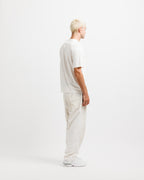 Cougar Milk | On Model Full Side A man with platinum blonde hair stands in profile wearing a white short-sleeve t-shirt, off-white cargo pants, and white sneakers against a seamless white studio background.