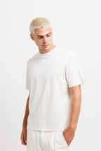 Cougar Milk | On Model Front A man with short blonde hair wearing a plain white crew-neck t-shirt and matching white trousers, standing against a solid white studio background.