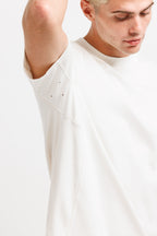 Cougar Milk | On Model Front Detail A close-up of a model wearing a white short-sleeve t-shirt with unique diagonal seam details and small perforations on the upper sleeve, set against a plain white background.