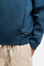 Stillwater Blue | On Model Detail Close-up of a person wearing a dark teal blue sweatshirt and beige drawstring pants, with the small multicolor XOX logo patch visible near the hem of the sweatshirt.