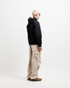 Ink Black | On Model Full Side A man with blonde hair and sunglasses is shown from a side-back angle wearing a black hoodie, beige cargo pants, and brown shoes against a plain white studio background.