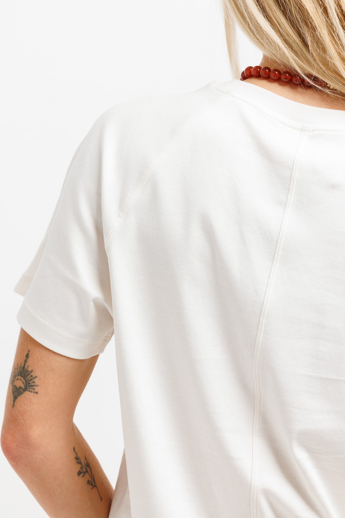 Close-up back view of a person wearing a plain white short-sleeve T-shirt against a light gray studio background.