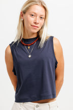 Deepwater Navy | A woman wearing a navy blue sleeveless crop top, styled with layered necklaces and light-colored pants, photographed against a clean white background.